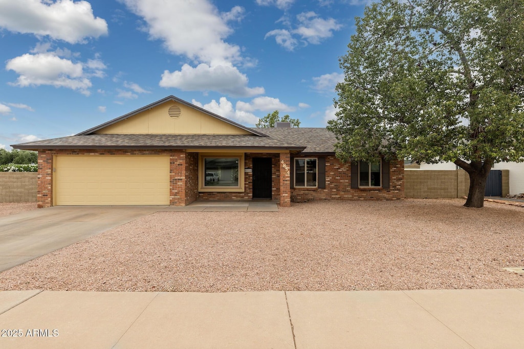 ranch-style house with driveway, an attached garage, fence, brick siding, and a shingled roof