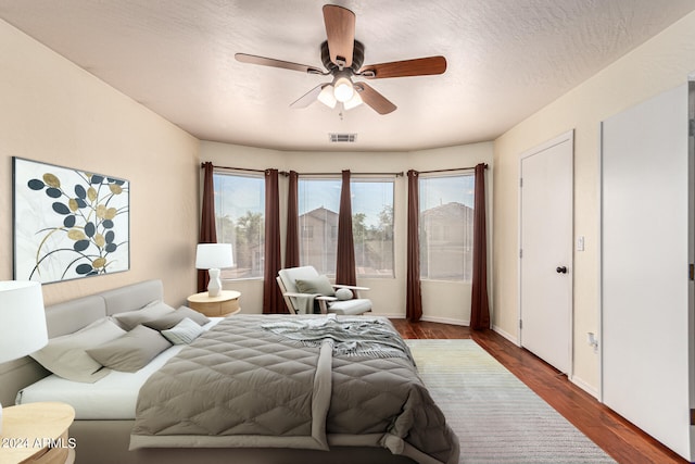 bedroom featuring ceiling fan, multiple windows, dark hardwood / wood-style flooring, and a textured ceiling