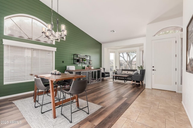 dining space featuring wood walls, an inviting chandelier, hardwood / wood-style flooring, and high vaulted ceiling