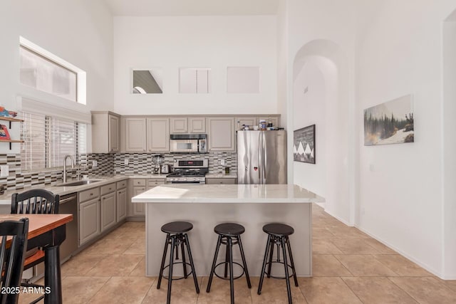 kitchen featuring a kitchen island, a kitchen bar, a towering ceiling, sink, and stainless steel appliances