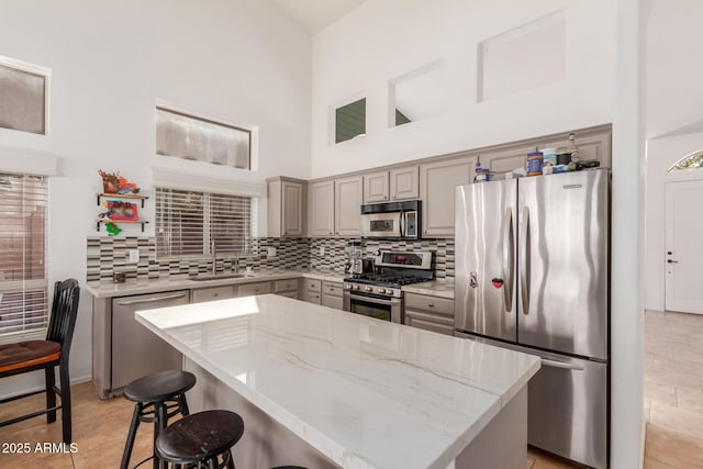 kitchen featuring a high ceiling, light stone countertops, a kitchen island, stainless steel appliances, and tasteful backsplash