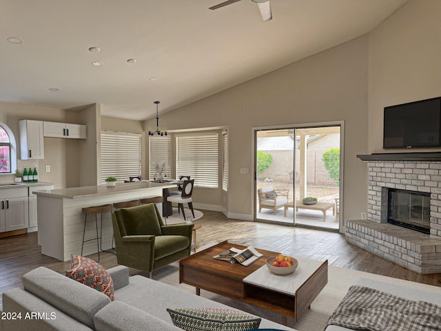 living room featuring vaulted ceiling, light wood-type flooring, ceiling fan with notable chandelier, and a brick fireplace