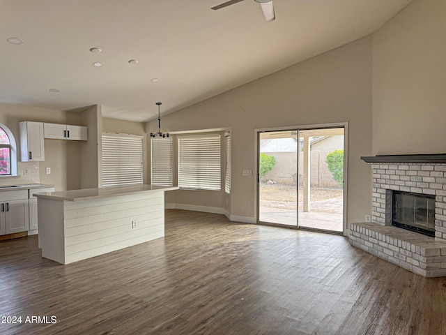 unfurnished living room featuring vaulted ceiling, a fireplace, ceiling fan with notable chandelier, and dark hardwood / wood-style floors