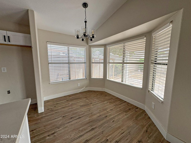 unfurnished dining area featuring a wealth of natural light, dark wood-type flooring, lofted ceiling, and an inviting chandelier