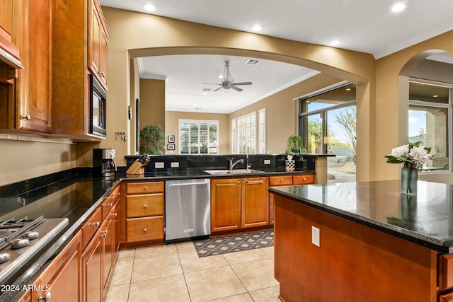 kitchen featuring ceiling fan, stainless steel appliances, ornamental molding, and dark stone counters