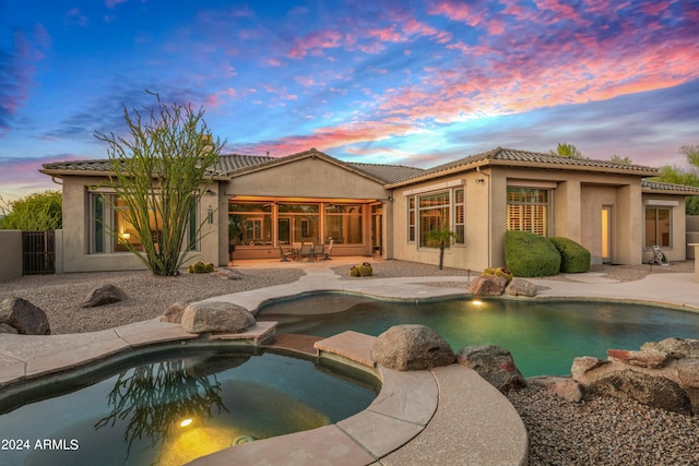 pool at dusk with an in ground hot tub and a patio