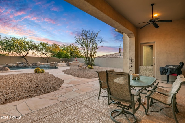 patio terrace at dusk with ceiling fan, a swimming pool with hot tub, and pool water feature