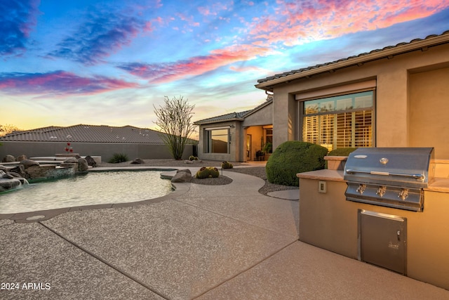 patio terrace at dusk featuring exterior kitchen and area for grilling