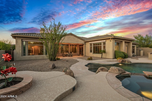 back house at dusk featuring a fenced in pool and a patio area