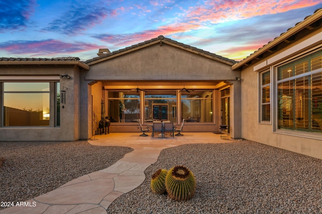 back house at dusk with ceiling fan and a patio