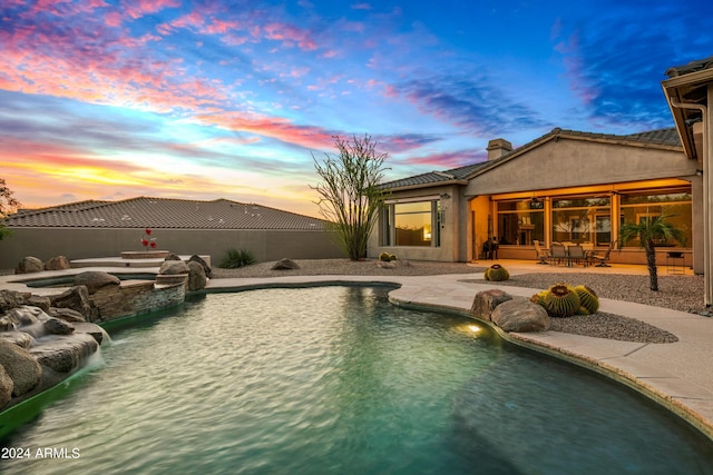 pool at dusk with an in ground hot tub, pool water feature, and a patio area