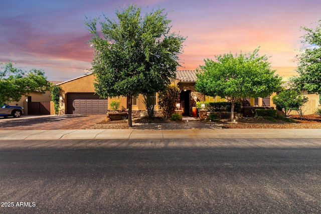 view of property hidden behind natural elements with stucco siding, an attached garage, a tile roof, decorative driveway, and stone siding