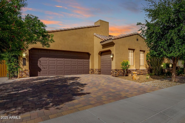 mediterranean / spanish-style home with a garage, a tile roof, stone siding, and decorative driveway