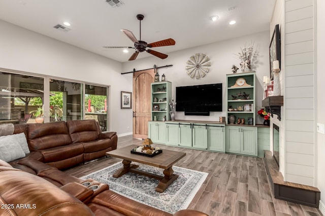 living area with light wood-style flooring, a barn door, visible vents, recessed lighting, and a ceiling fan
