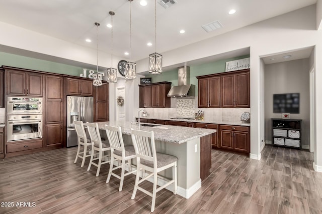 kitchen featuring wood finished floors, wall chimney exhaust hood, stainless steel appliances, and a sink
