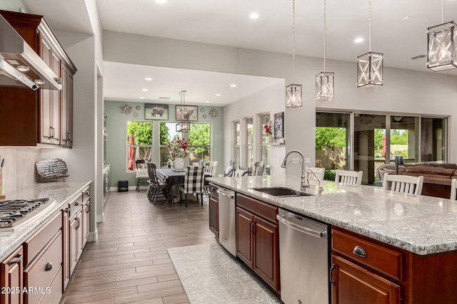 kitchen featuring wall chimney exhaust hood, a sink, open floor plan, recessed lighting, and appliances with stainless steel finishes
