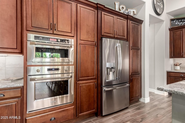kitchen featuring baseboards, appliances with stainless steel finishes, light stone countertops, and light wood-style flooring