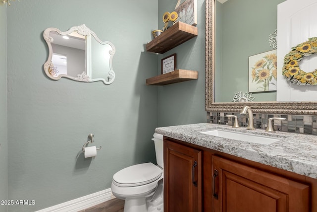 half bath featuring wood finished floors, toilet, vanity, baseboards, and tasteful backsplash