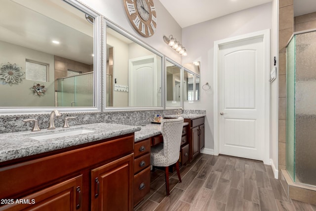full bathroom with wood finished floors, a sink, double vanity, and a stall shower