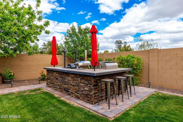 view of patio with outdoor wet bar, area for grilling, a fenced backyard, and a grill
