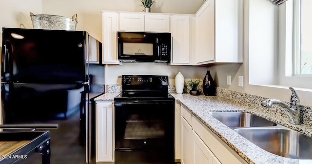 kitchen with light stone counters, sink, white cabinets, and black appliances