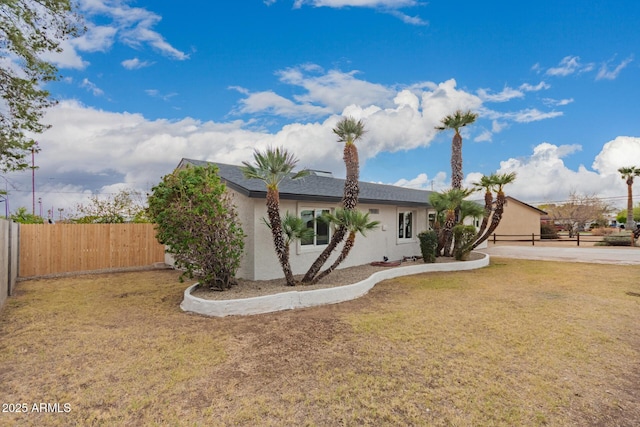 view of front of house featuring stucco siding, a front lawn, and fence