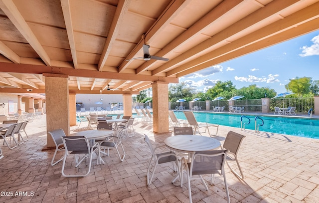 view of patio featuring ceiling fan, outdoor dining space, fence, and a community pool