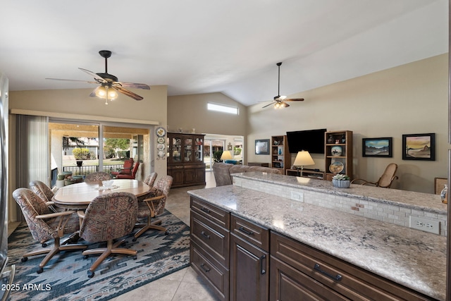 kitchen featuring lofted ceiling, light tile patterned flooring, open floor plan, dark brown cabinets, and light stone countertops