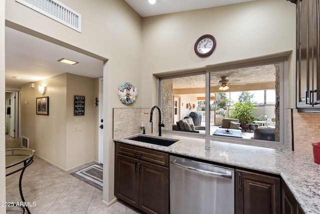 kitchen featuring dark brown cabinetry, light stone countertops, a sink, stainless steel dishwasher, and decorative backsplash