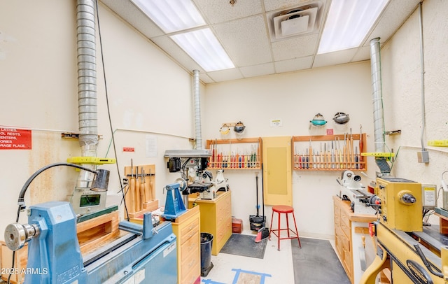 misc room featuring concrete floors, a workshop area, a drop ceiling, and visible vents