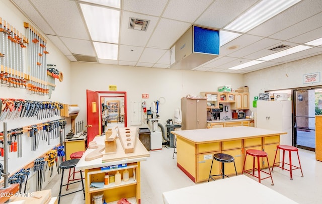 kitchen featuring visible vents, a drop ceiling, a breakfast bar, a center island, and light countertops