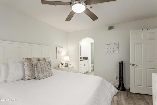 bedroom featuring visible vents, arched walkways, connected bathroom, light wood-style flooring, and ceiling fan