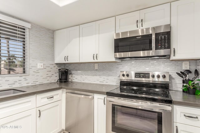 kitchen featuring stainless steel appliances, dark countertops, white cabinetry, and backsplash