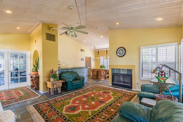 living area featuring high vaulted ceiling, wooden ceiling, visible vents, and a tiled fireplace