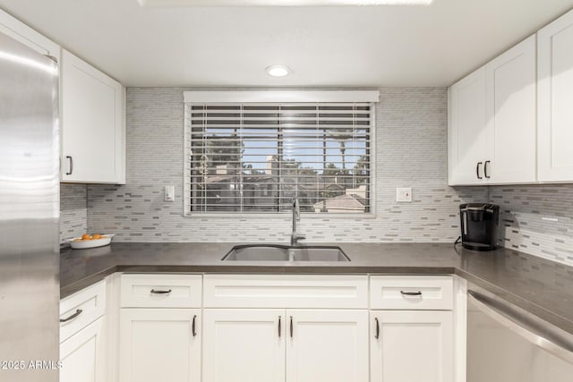 kitchen featuring dark countertops, backsplash, appliances with stainless steel finishes, white cabinets, and a sink