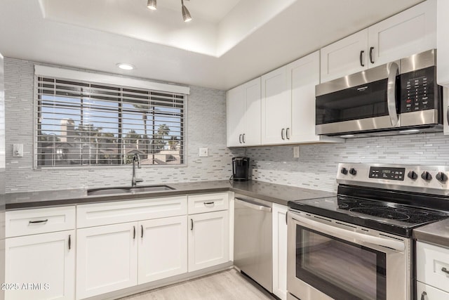 kitchen featuring dark countertops, backsplash, appliances with stainless steel finishes, white cabinetry, and a sink