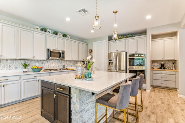 kitchen with appliances with stainless steel finishes, white cabinets, a center island, light hardwood / wood-style floors, and hanging light fixtures