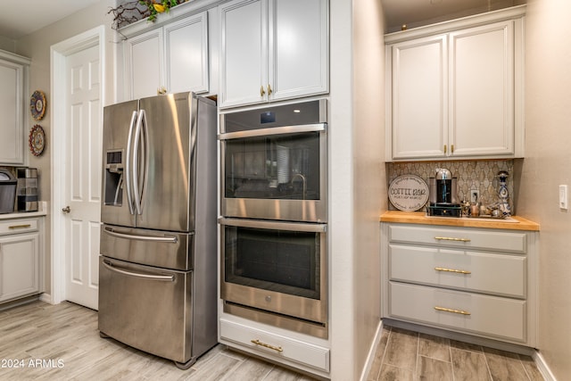 kitchen featuring butcher block countertops, backsplash, stainless steel appliances, and light hardwood / wood-style flooring