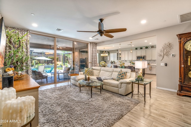 living room with ceiling fan with notable chandelier and light hardwood / wood-style flooring