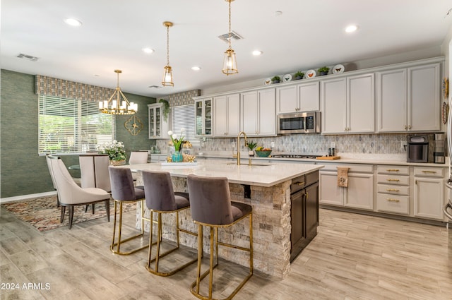 kitchen with sink, a healthy amount of sunlight, decorative light fixtures, a kitchen island with sink, and appliances with stainless steel finishes