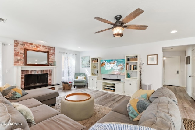 living room featuring a brick fireplace, light hardwood / wood-style flooring, and ceiling fan