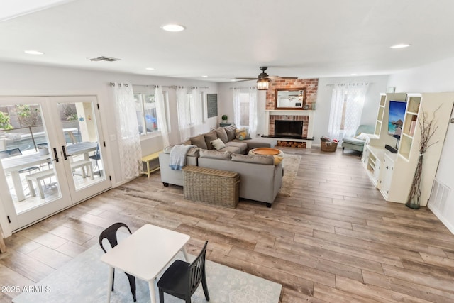 living room featuring french doors, a brick fireplace, ceiling fan, and light hardwood / wood-style flooring