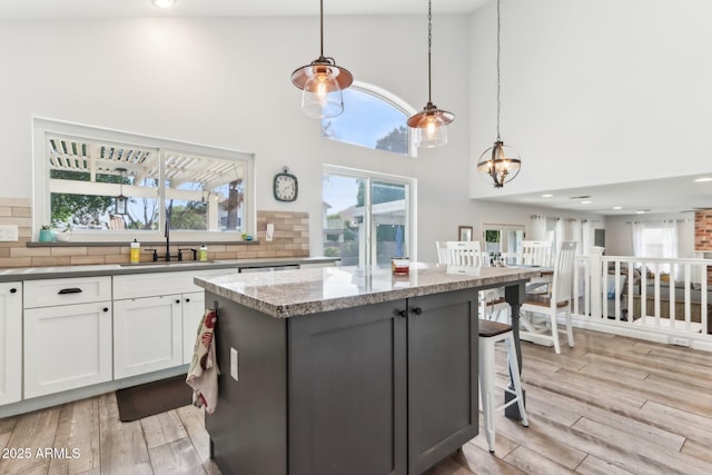 kitchen featuring sink, white cabinetry, a center island, dark stone countertops, and pendant lighting