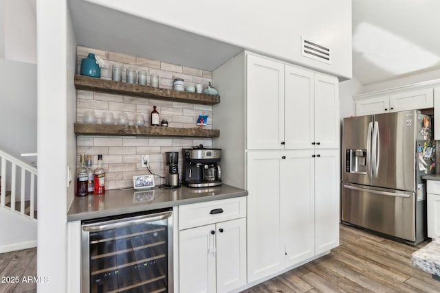 bar with tasteful backsplash, white cabinets, beverage cooler, stainless steel fridge with ice dispenser, and light hardwood / wood-style flooring