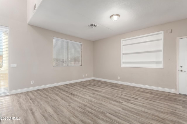 spare room with built in shelves, visible vents, baseboards, and wood finished floors