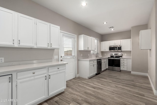 kitchen with appliances with stainless steel finishes, white cabinetry, and light wood finished floors