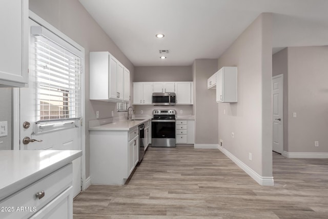 kitchen featuring stainless steel appliances, a sink, baseboards, white cabinets, and light wood-type flooring