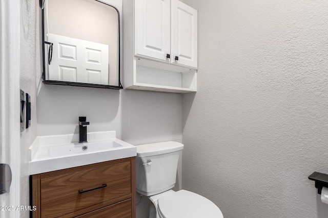 half bath with a textured wall, vanity, and toilet