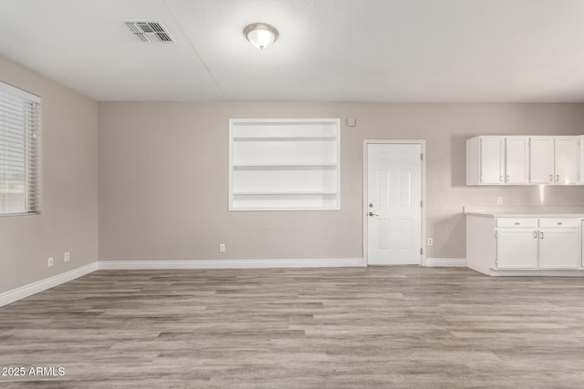 interior space featuring baseboards, built in shelves, visible vents, and light wood-style floors