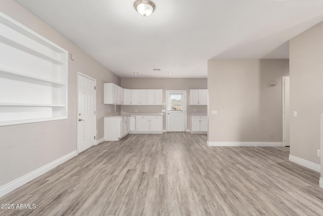 unfurnished living room featuring light wood-type flooring, built in features, visible vents, and baseboards